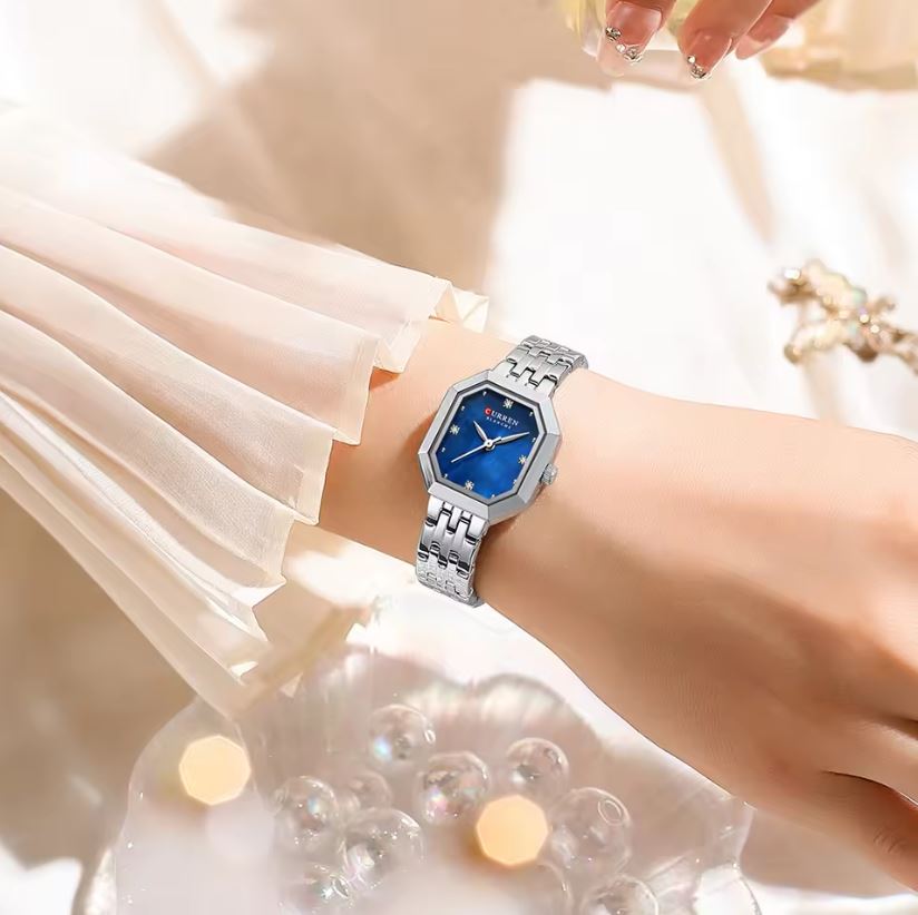 Wristwatch with blue face and silver band on a wrist, blurred background