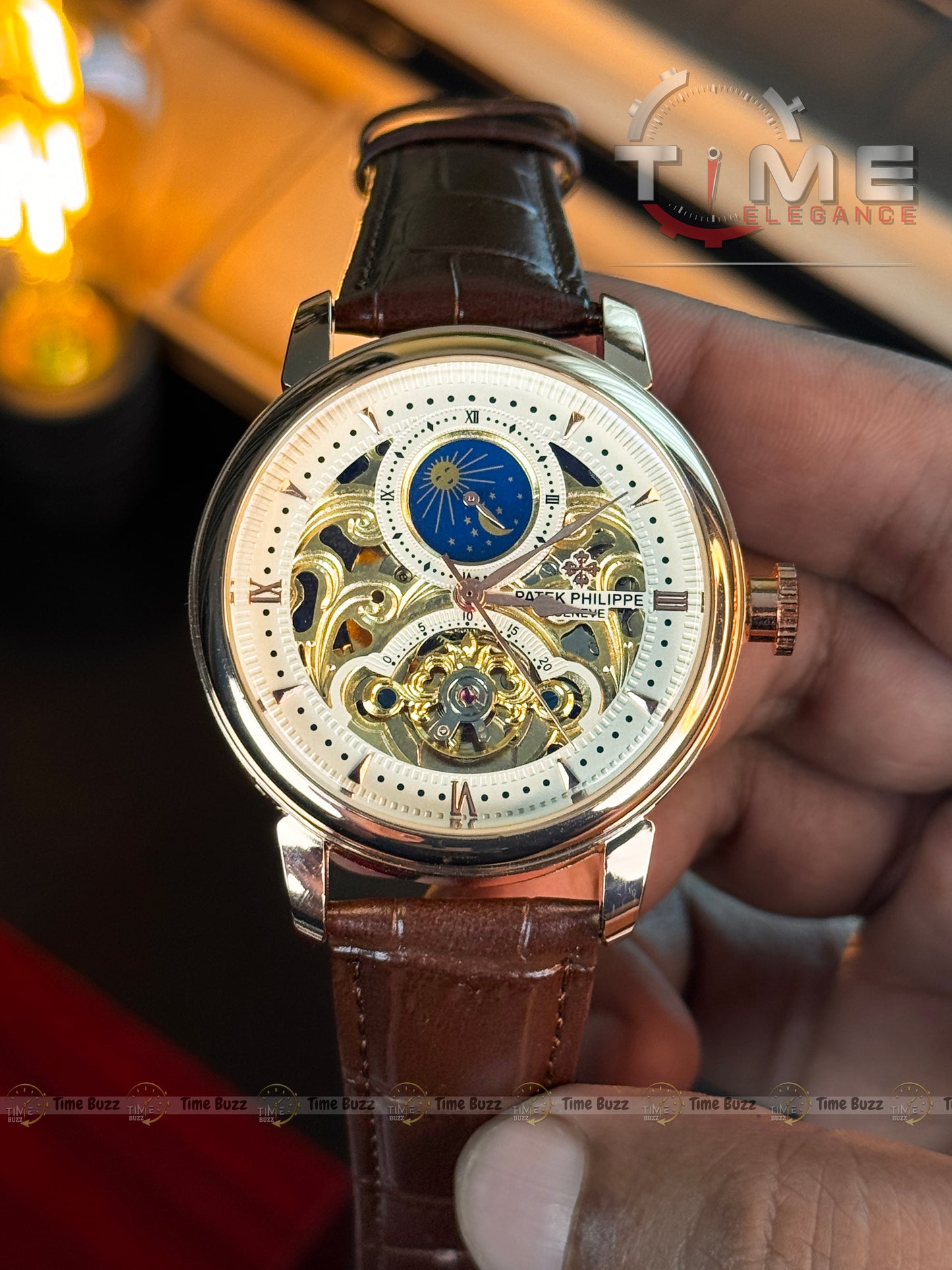 A luxury skeleton watch with a brown leather strap, held by a hand. The watch features a white dial with gold-tone gears, a blue moonphase indicator, and a polished gold-toned case.