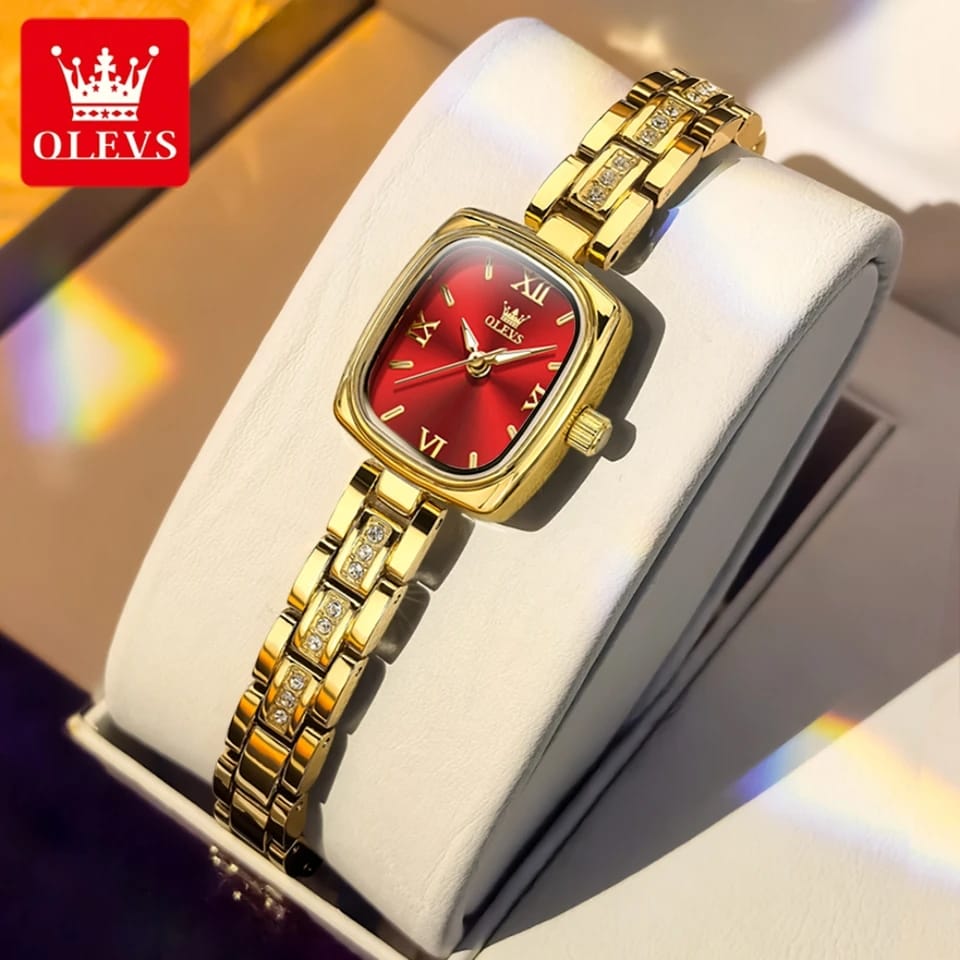 Gold watch with red face on a white cushion, OLEVS brand visible