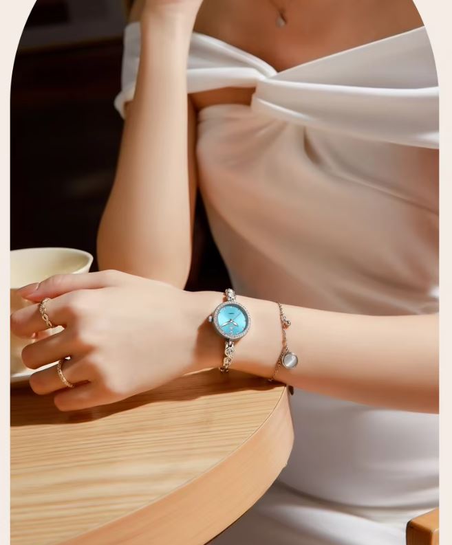 Person wearing a watch with a blue face and white strap, holding a cup.
