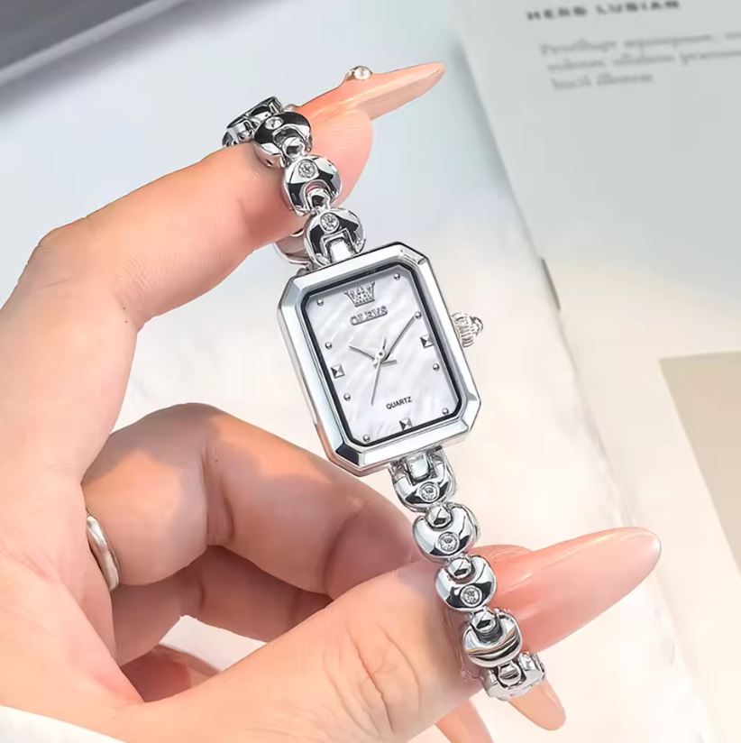 Silver bracelet watch held by a hand with a blurred background