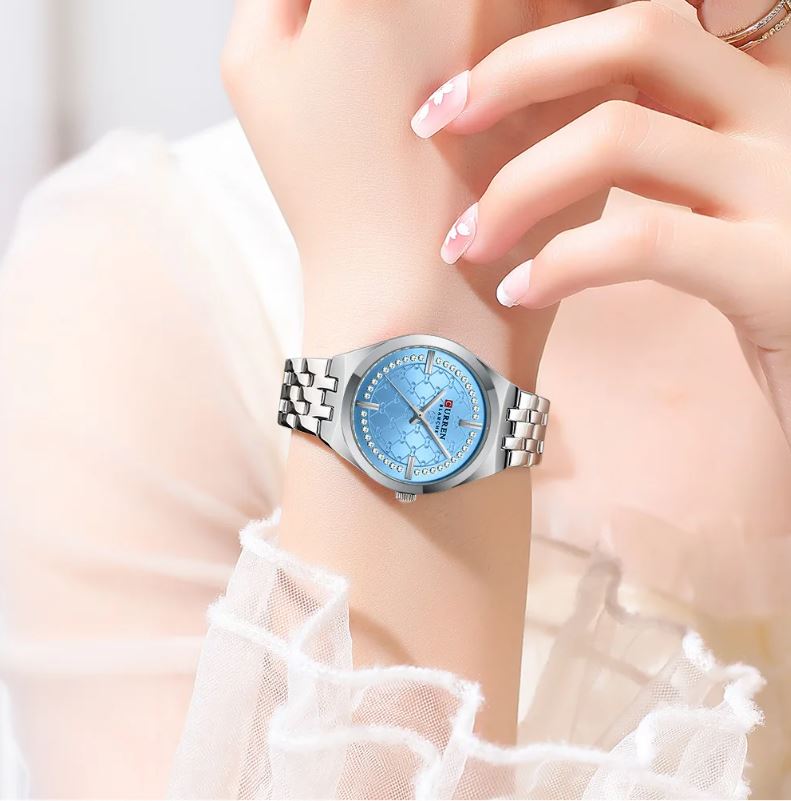 Wristwatch with a blue face on a wrist, wearing a white lace garment.