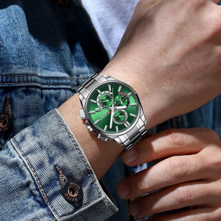 Green watch with silver case on a person's wrist wearing a denim jacket.