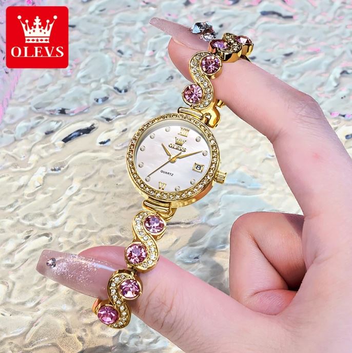 Gold and pink gemstone watch held by a hand with a glittery background