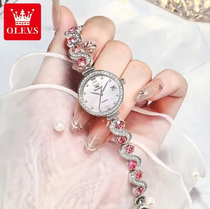 Hand holding a silver watch with pink gemstones on a white background, featuring the OLEVS brand.