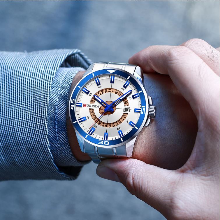 Hand wearing a watch with a blue and white face, blurred background