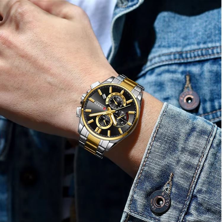 Close-up of a person's wrist wearing a gold and silver watch with a denim jacket.