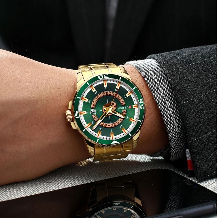 Gold and green watch on a person's wrist with a dark suit background