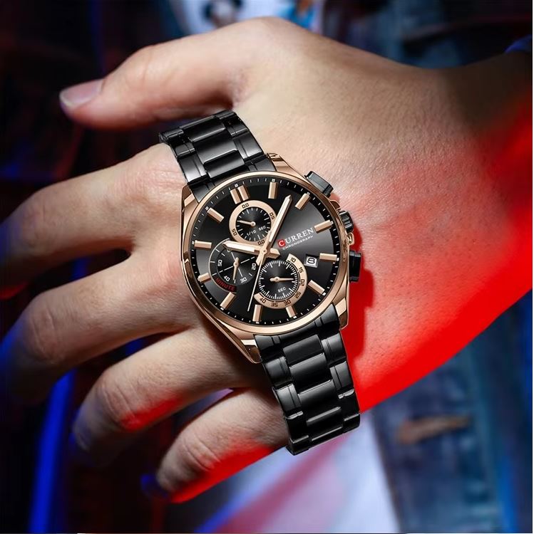 Hand wearing a black and rose gold watch with a blurred background
