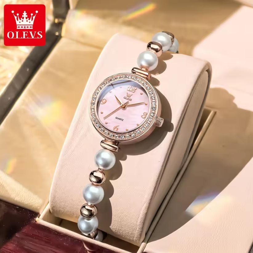 Wristwatch with pearl-like beads on a beige cushion, brand 'OLEVS' visible