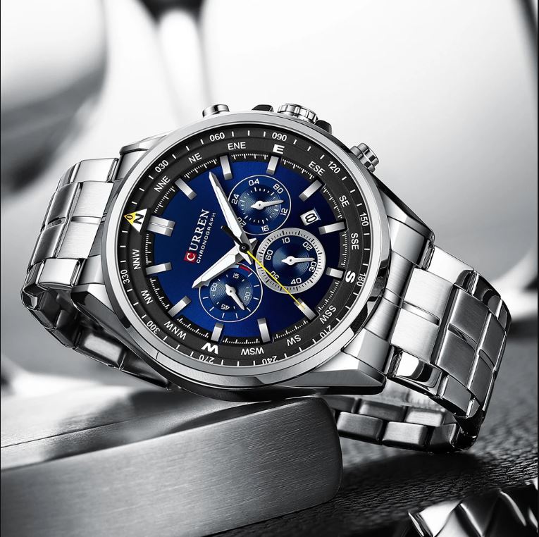 Silver wristwatch with a blue face on a reflective surface