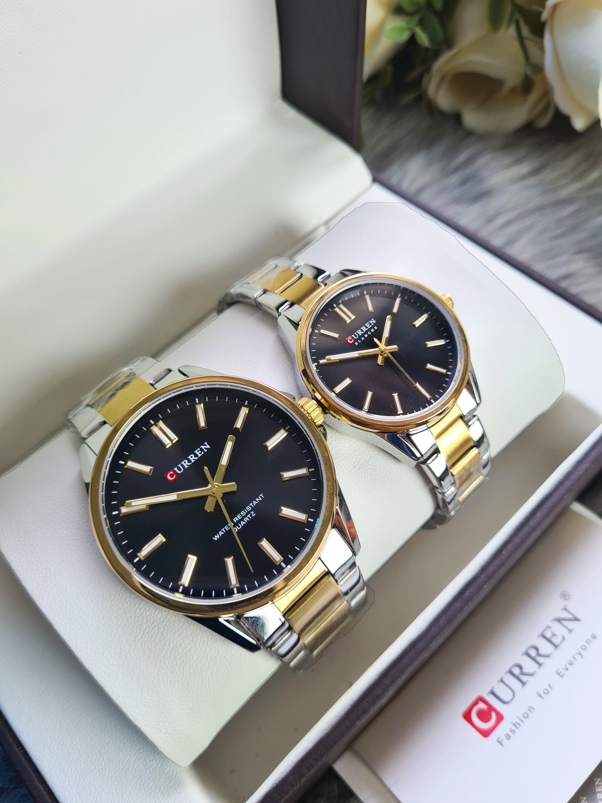 Two watches with black faces and gold accents on a white surface, with 'Curren' branding visible.