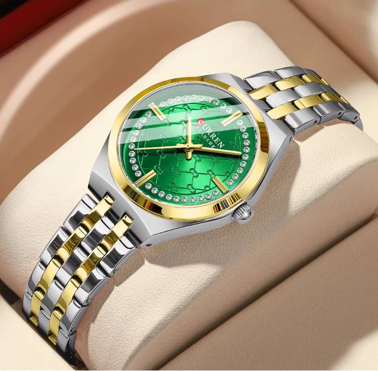 Luxury watch with green face and gold and silver band on beige surface