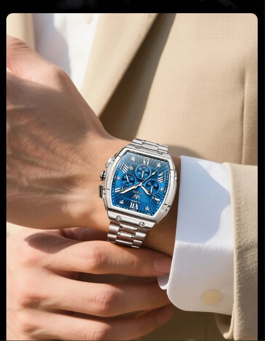 Hand wearing a silver watch with a blue face, dressed in a beige suit and white shirt.