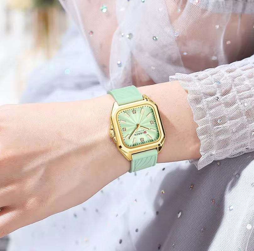 Green watch with gold case on a wrist, wearing a white lace garment.