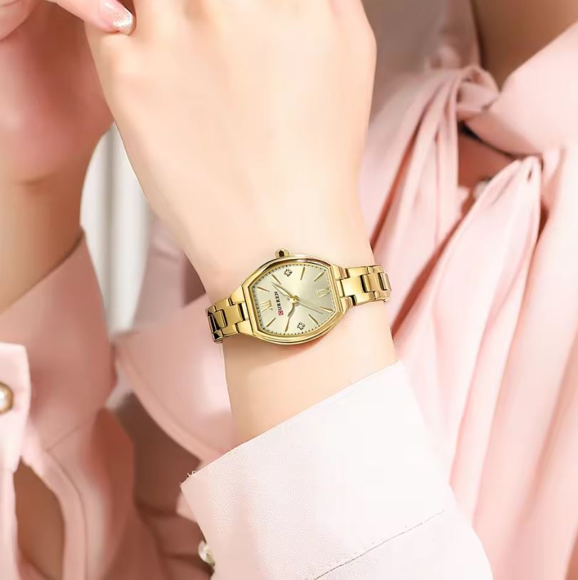 Gold wristwatch on a person's wrist with a soft pink background