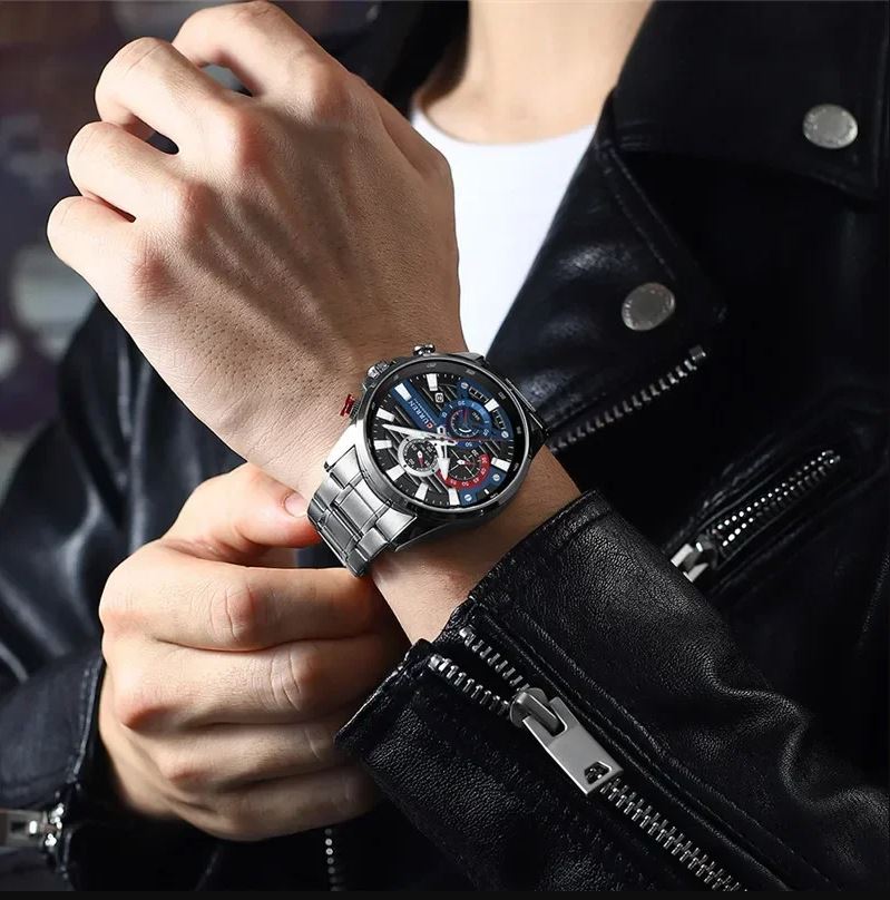 Person wearing a silver wristwatch with a black leather strap on a blurred background