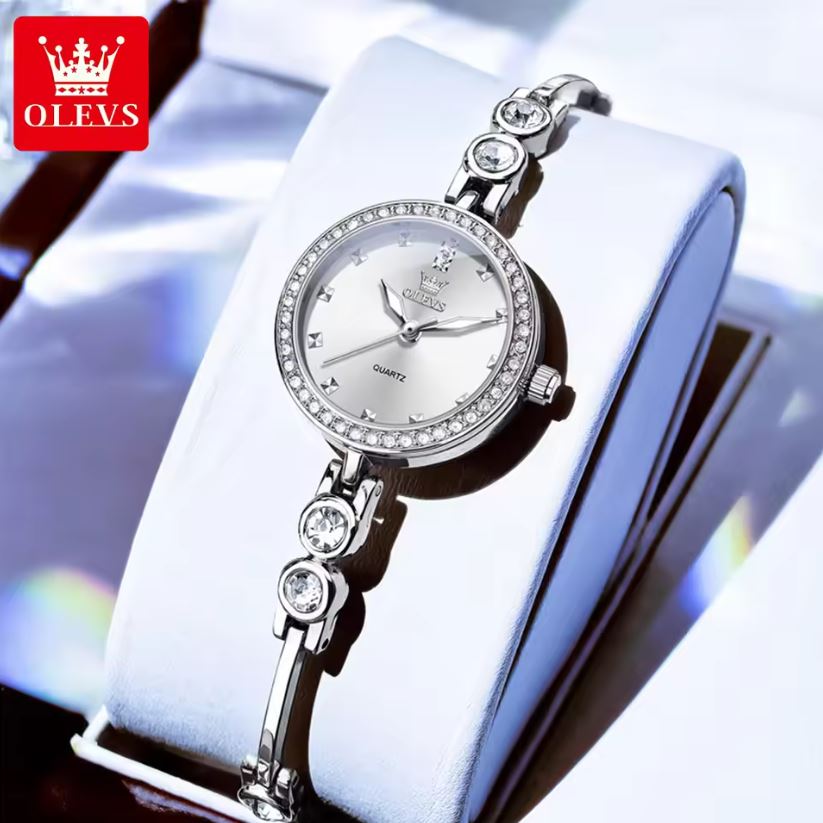 Silver wristwatch with diamond accents on a white box, branded 'OLEVS'.