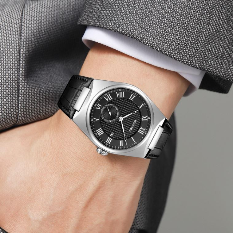 Close-up of a wrist wearing a black and silver watch with a gray suit background