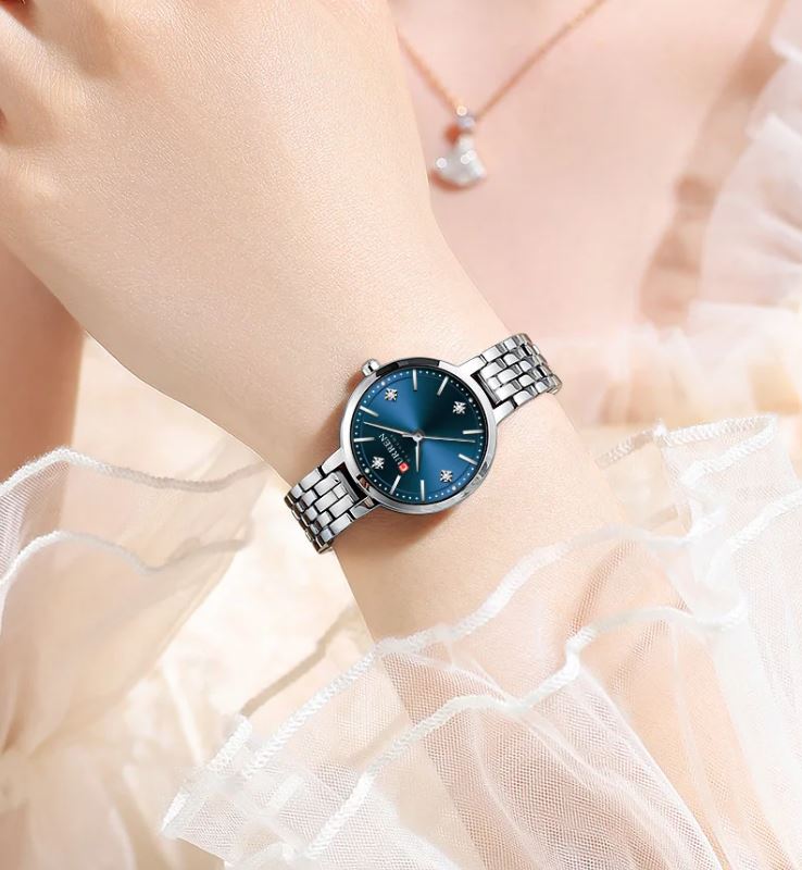 Silver watch with a blue face on a wrist, wearing a white lace garment.