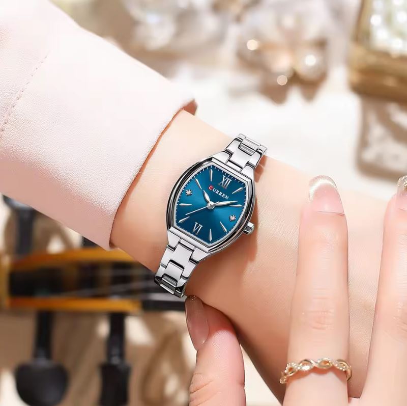 Silver watch with a blue face on a wrist, blurred background