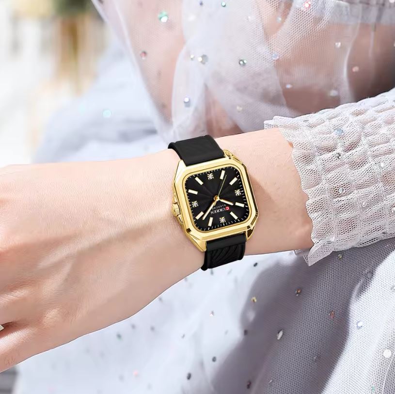 Gold watch with black strap on a wrist against a blurred background