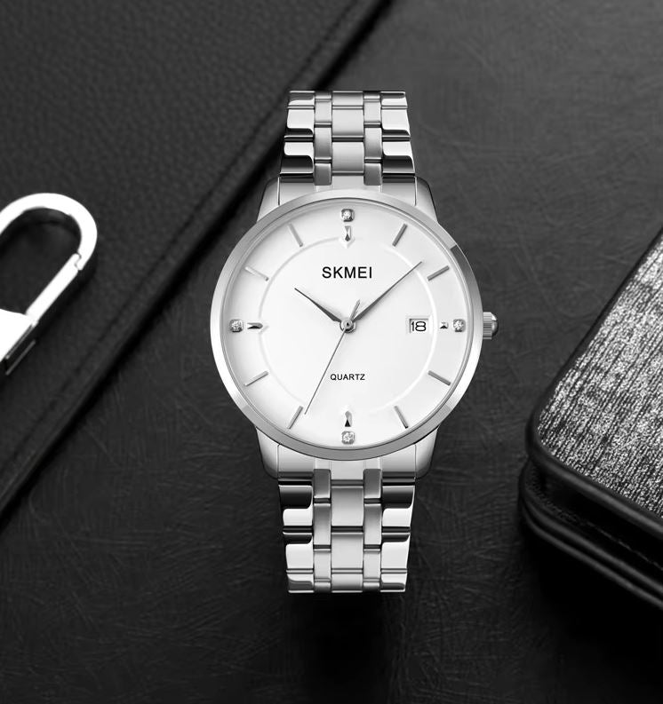 Silver SKMEI watch on a dark surface with a phone and pen.
