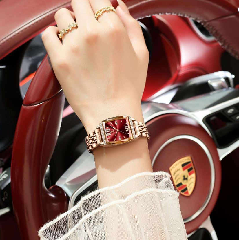 Hand wearing a gold watch with a red face in front of a car interior.