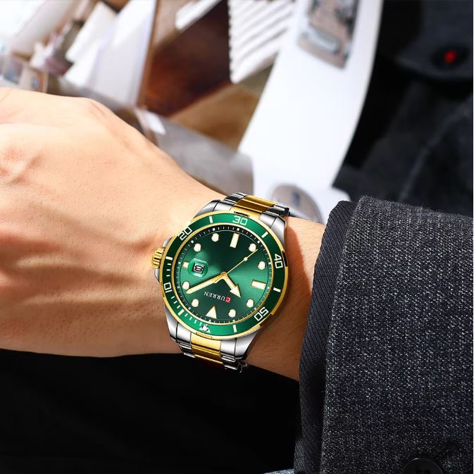 Green watch with gold accents on a wrist, blurred indoor background