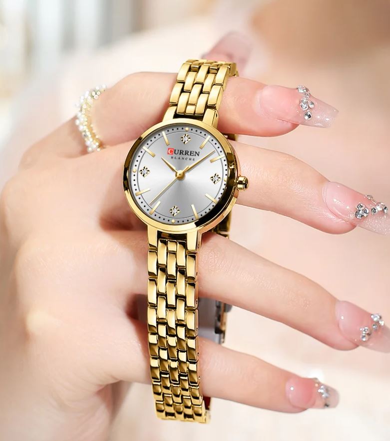 Gold wristwatch held by a hand with decorative nails on a blurred background
