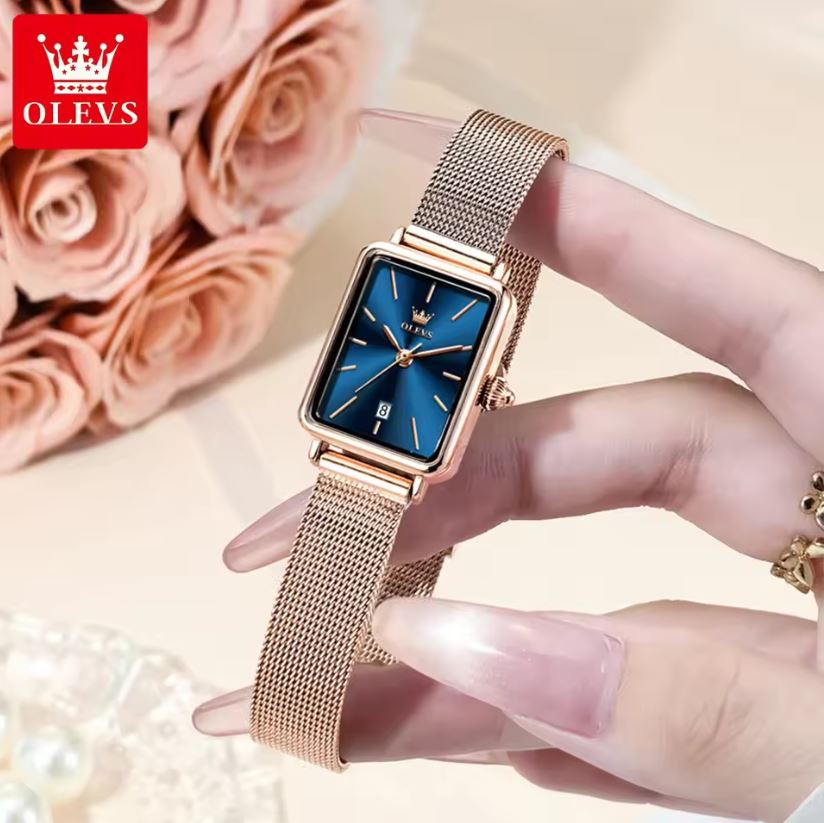 Rose gold watch with blue face held by a hand, OLEVS brand visible, with pink roses in the background.