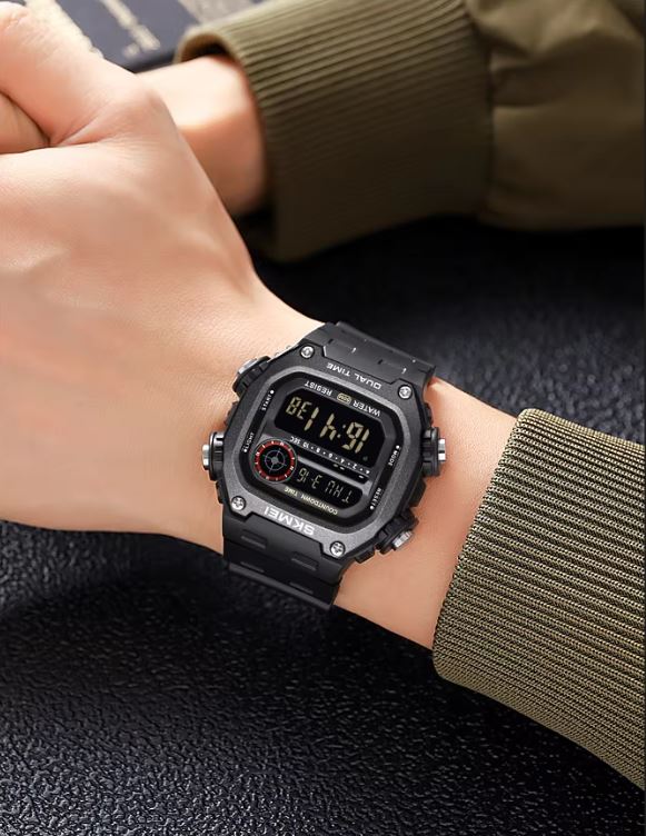 Black digital wristwatch on a person's wrist with a green sleeve.