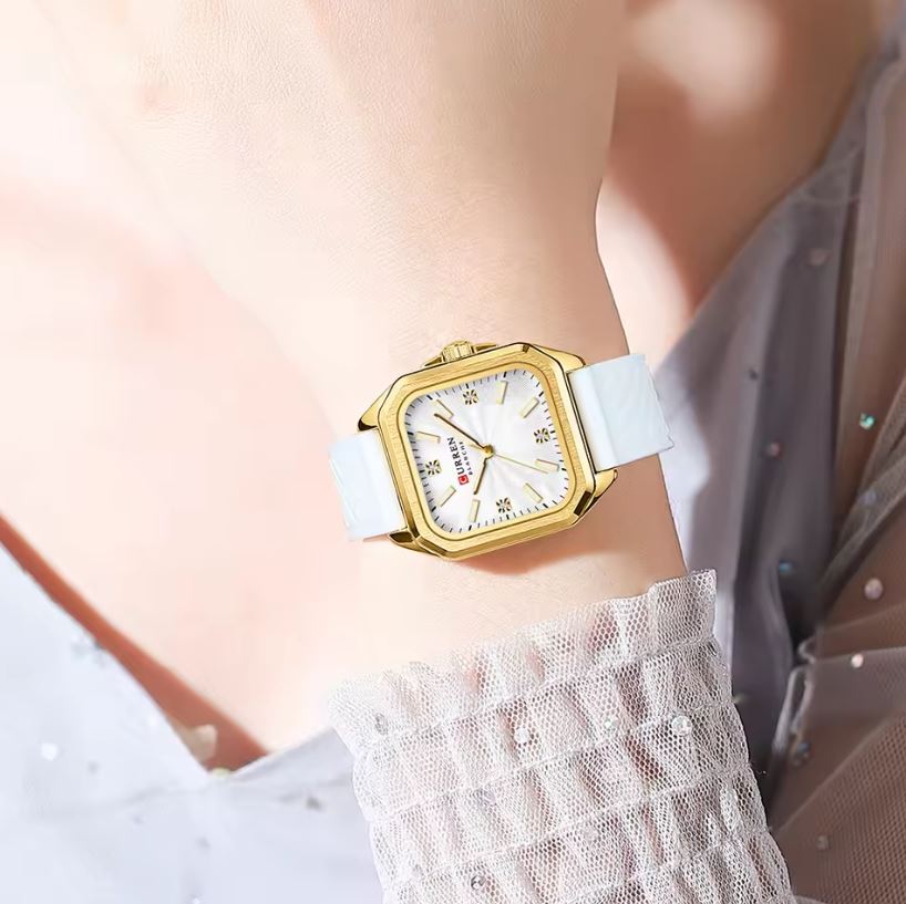 Gold watch with a white strap on a person's wrist against a neutral background
