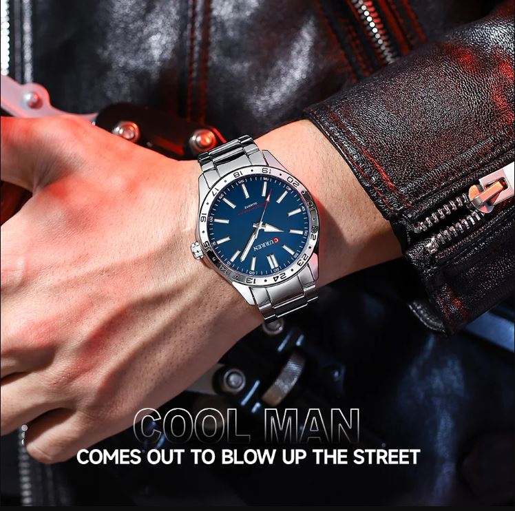 Person wearing a silver watch with a blue face on a dark background