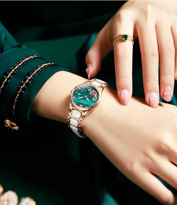 Close-up of a hand wearing a green wristwatch with a gold strap on a dark background