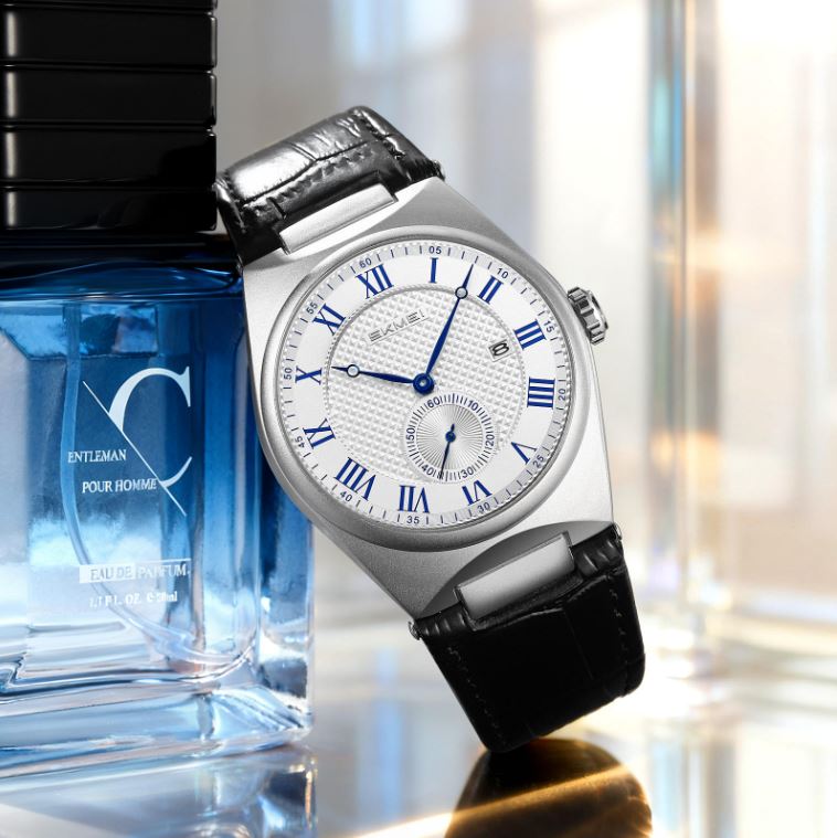 Silver watch with black leather strap next to a blue bottle of cologne.