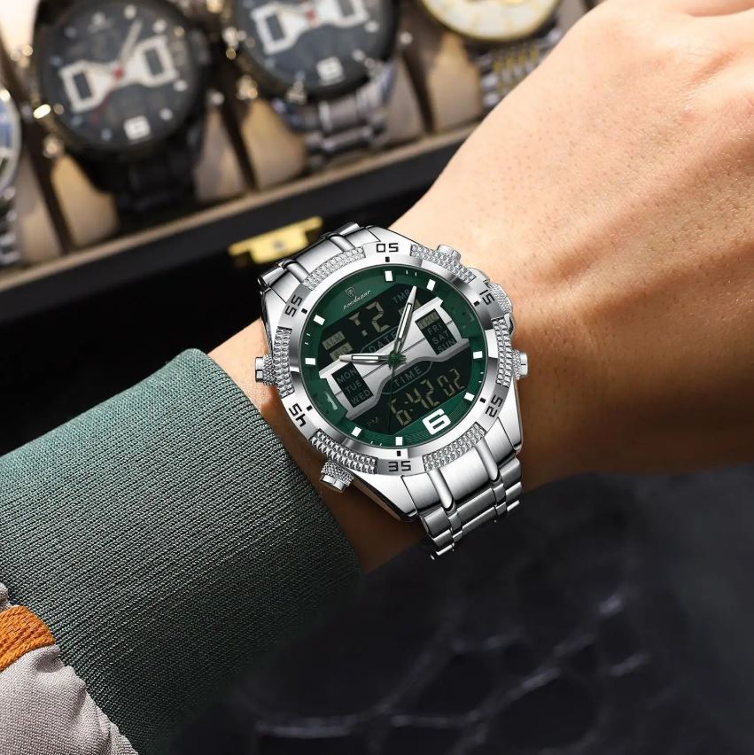 Silver watch with green face on a wrist, with a blurred background of other watches.