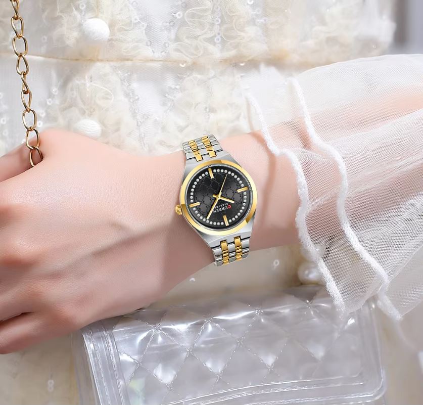 Gold and silver watch on a wrist with a white lace garment in the background