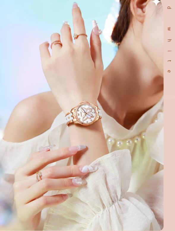Close-up of a woman's hand wearing a rose gold watch with a white strap against a soft, blurred background.