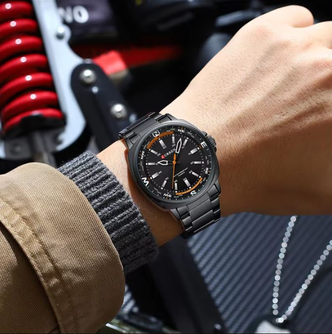 Person wearing a black wristwatch with a motorcycle in the background