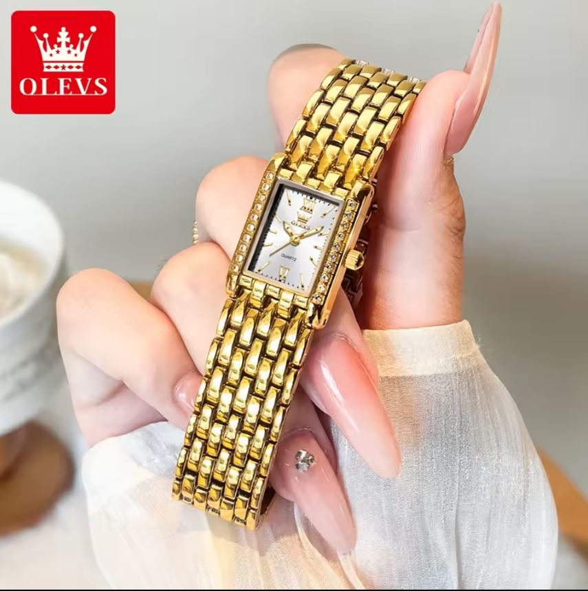 Gold watch held by a hand with a blurred background