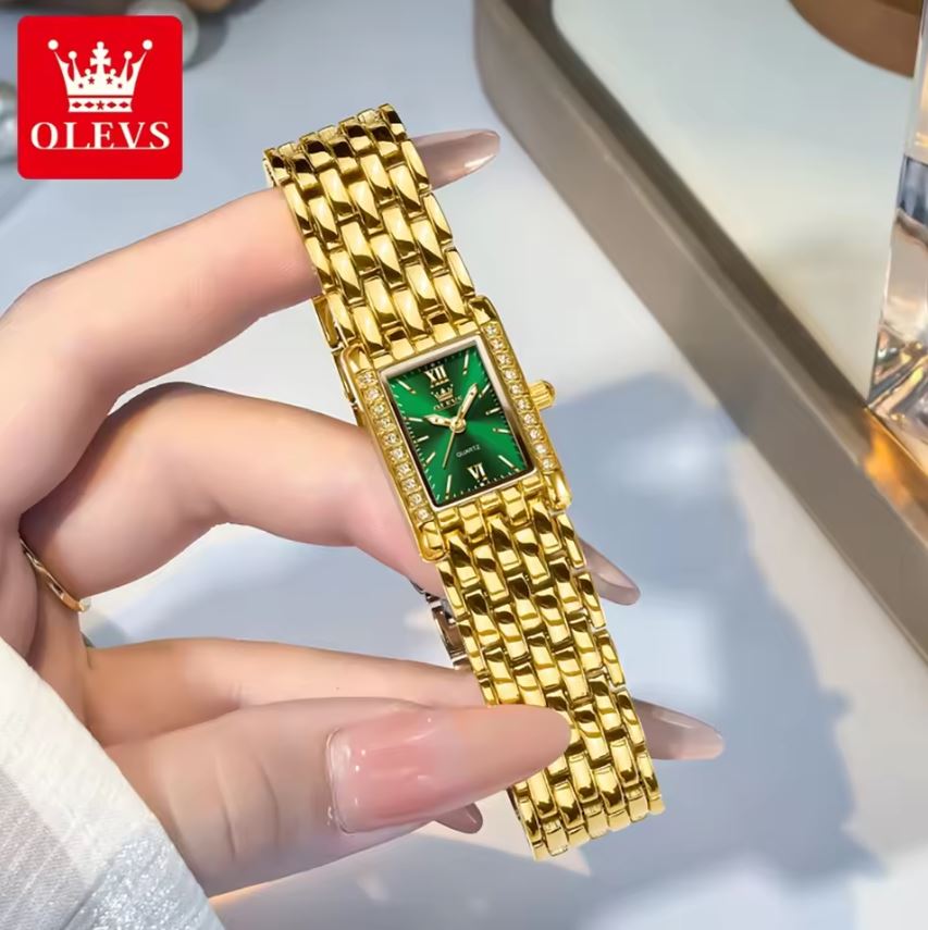 Gold watch with green face held by a hand, OLEVS brand visible