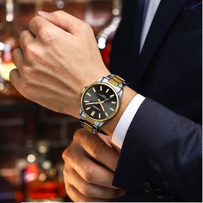 Close-up of a person wearing a gold and black watch with a blurred background