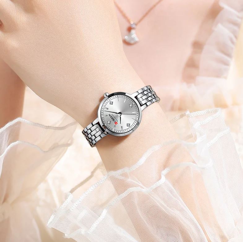 Silver wristwatch on a person wearing a white dress with ruffled sleeves.
