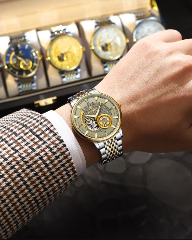 Hand wearing a gold and silver watch with a display of watches in the background