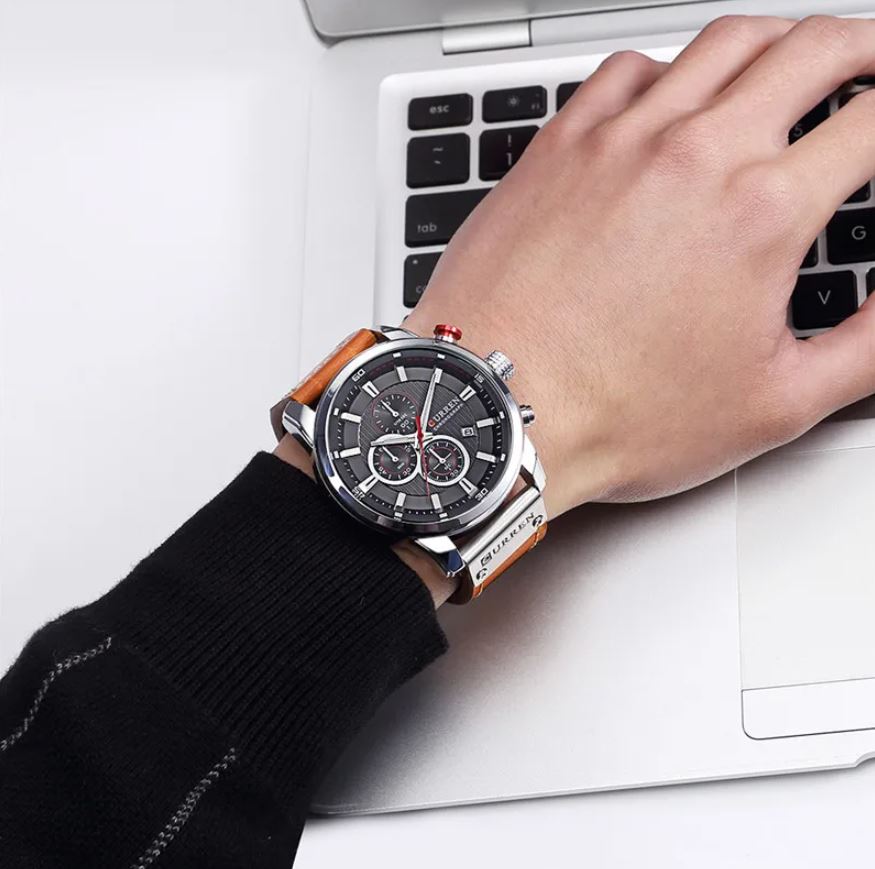 Hand wearing a watch with a laptop in the background