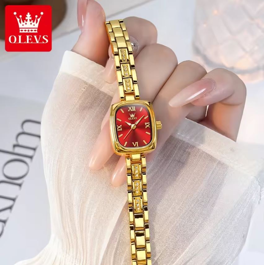 Gold watch with red face held by a hand, brand 'OLEVS' visible