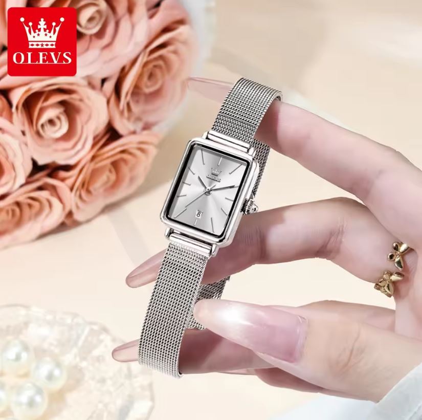 Silver watch held by a hand with pink roses and pearls in the background, featuring the OLEVS brand.