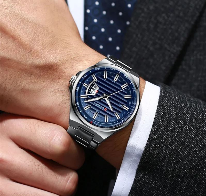 Close-up of a person wearing a watch with a blue face and silver case, dressed in formal attire.