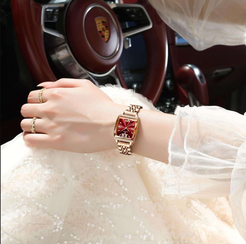 Hand wearing a gold watch with a red face in a car interior.